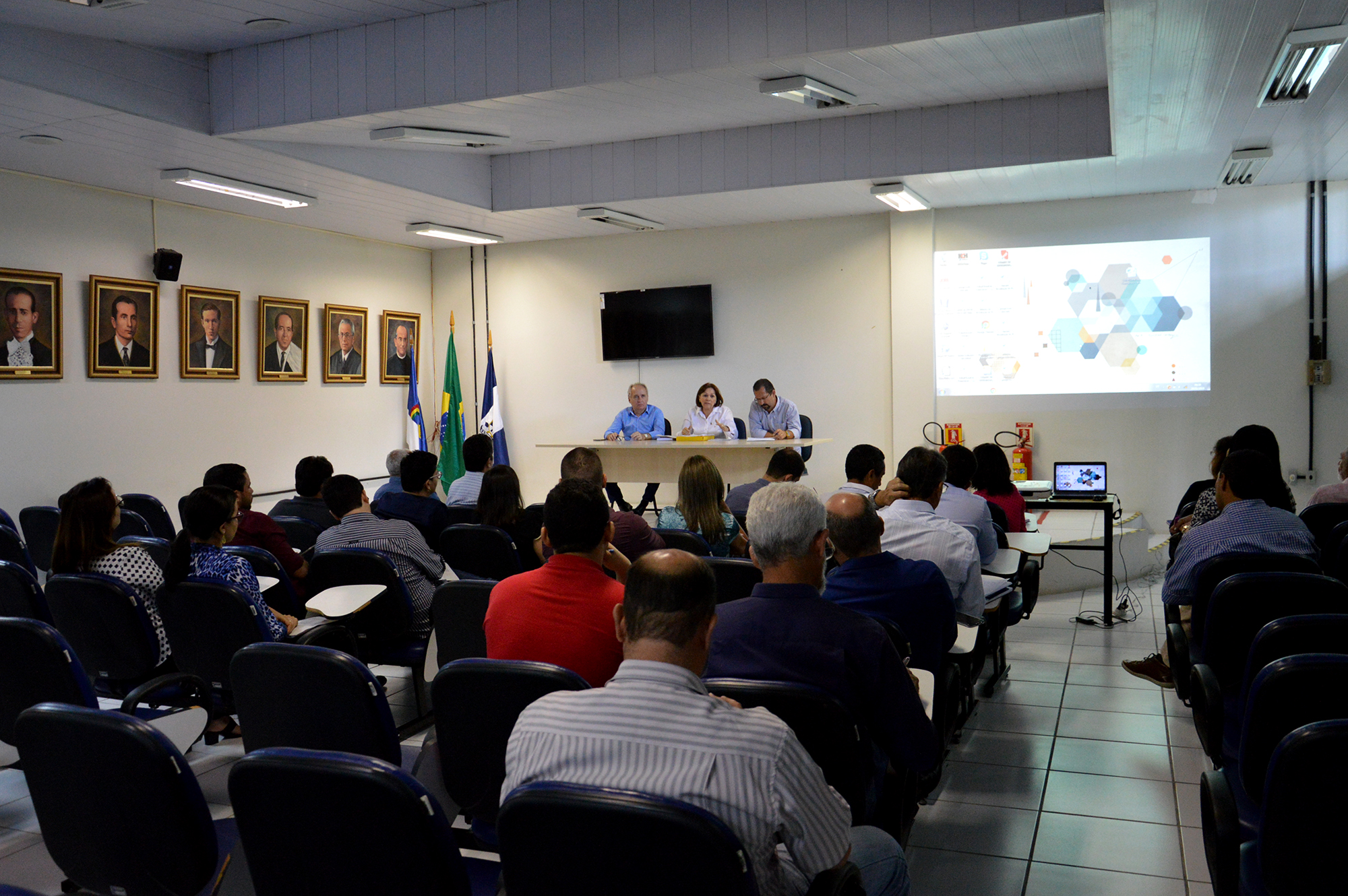 Pessoas sentadas em auditório ouvindo participantes da mesa de debate sentados à mesa